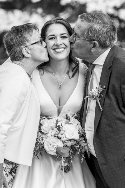 Mariée entourée de ses parents lui faisant un bisou sur la joue pendant son mariage à Annecy