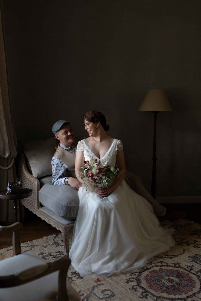 mariée assisse avec u bouquet dans ses bras regardant son mari qui porte une casquette